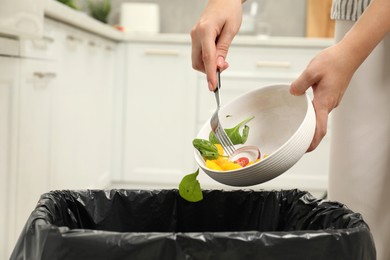 Photo of Woman throwing vegetable salad into bin indoors, closeup