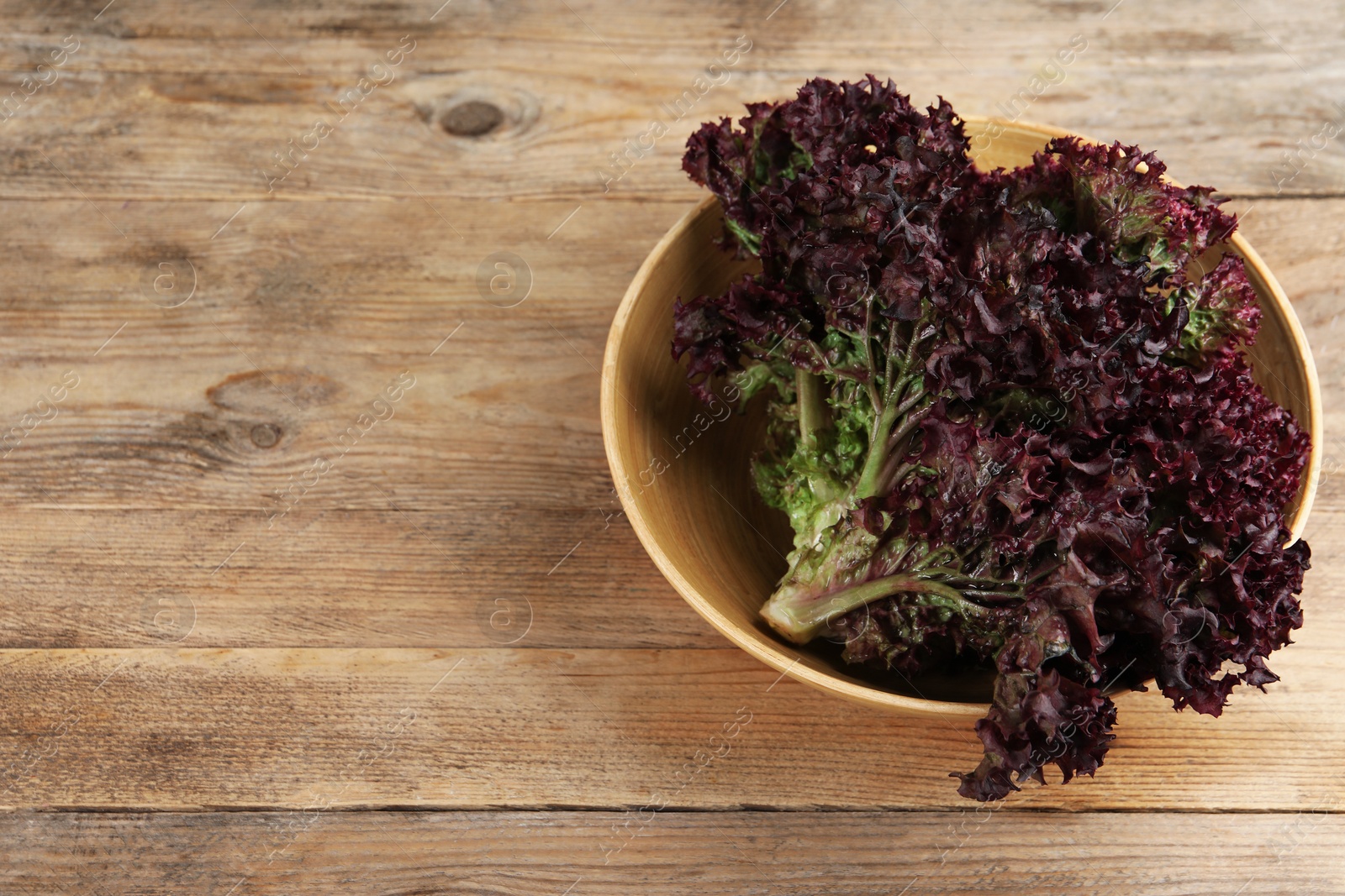 Photo of Bowl of fresh red coral lettuce on wooden table, above view with space for text