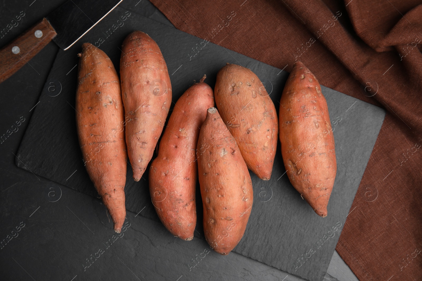 Photo of Heap of whole ripe sweet potatoes on black table, flat lay