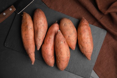 Photo of Heap of whole ripe sweet potatoes on black table, flat lay