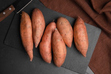 Heap of whole ripe sweet potatoes on black table, flat lay