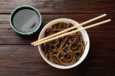 Photo of Tasty buckwheat noodles (soba), chopsticks and sauce on wooden table, flat lay