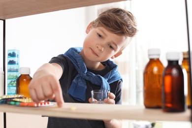 Photo of Little child taking pills from shelf at home. Danger of medicament intoxication