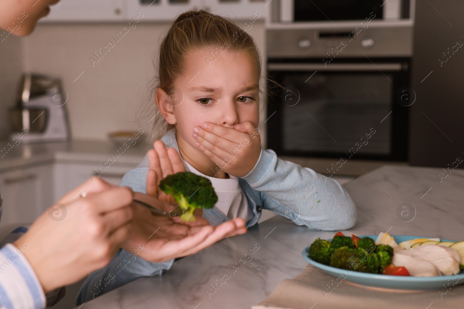 Photo of Mother feeding her daughter in kitchen, closeup. Little girl refusing to eat dinner