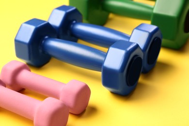 Many different dumbbells on yellow background, closeup