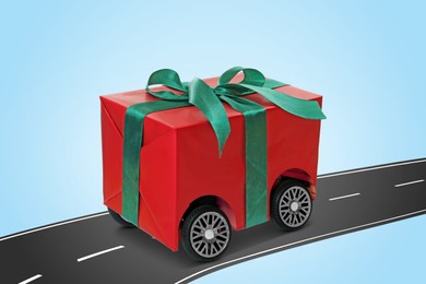 Gift box with wheels riding on asphalt road against light blue background. Delivery service