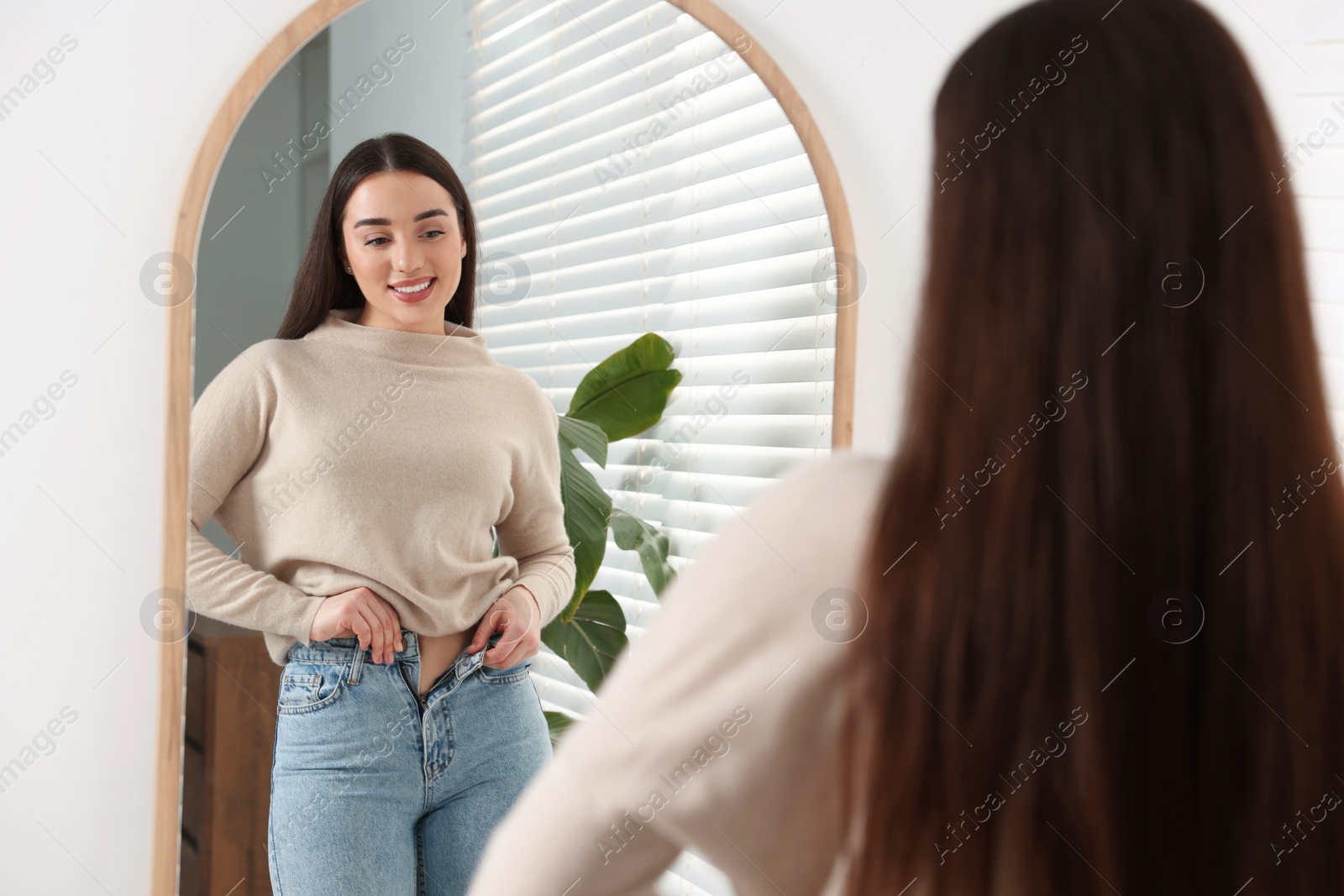 Photo of Young woman in stylish jeans near mirror indoors