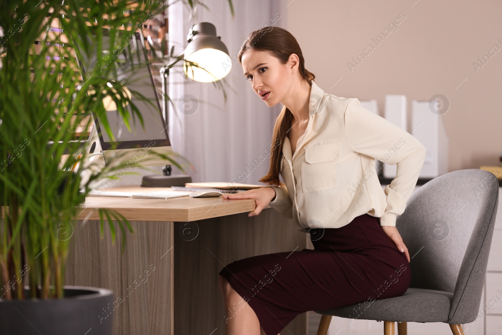 Photo of Young woman suffering from hemorrhoid at workplace in office