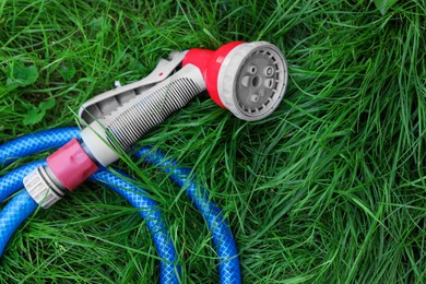Watering hose with sprinkler on green grass outdoors, top view