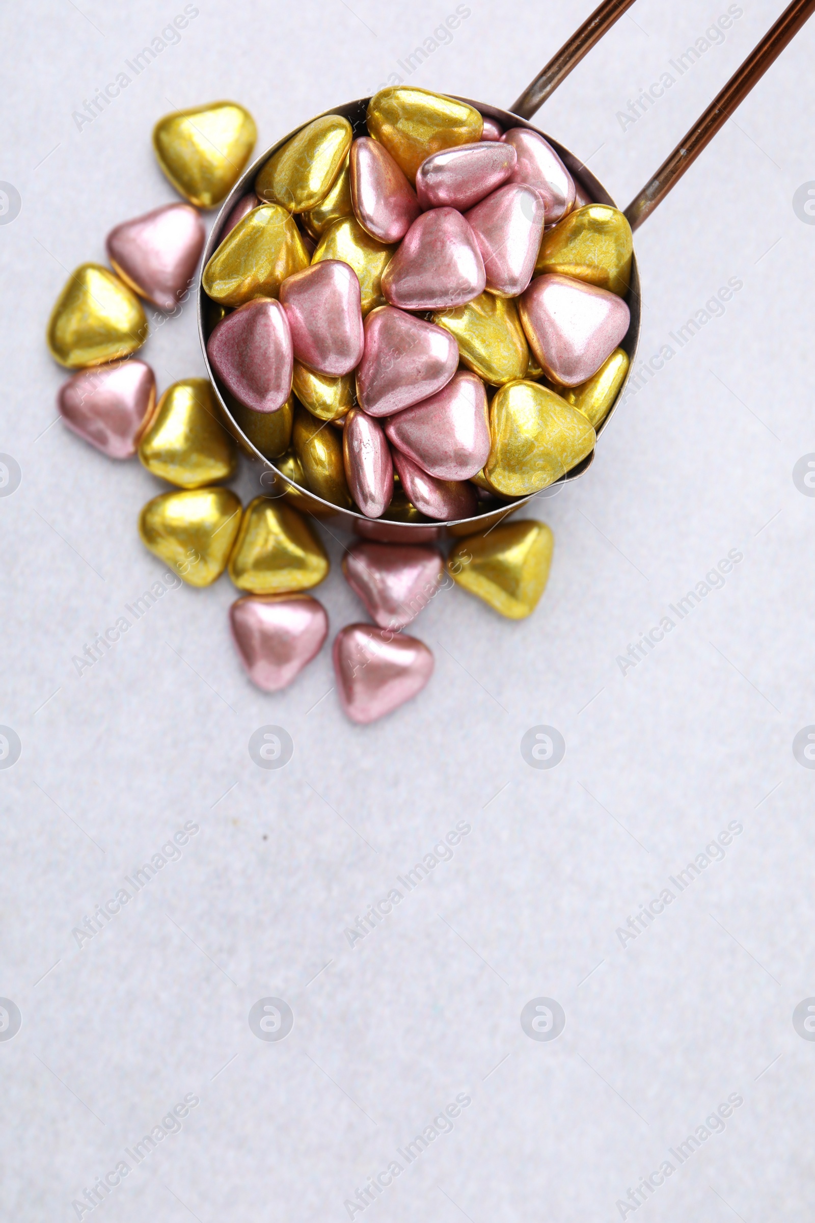 Photo of Metal scoop and delicious heart shaped candies on white table, flat lay. Space for text