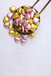 Metal scoop and delicious heart shaped candies on white table, flat lay. Space for text