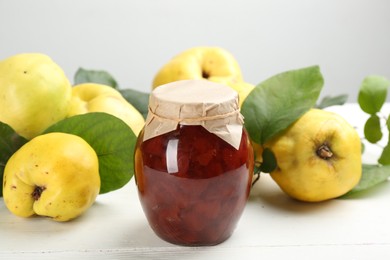 Photo of Delicious quince jam and fruits on white wooden table, closeup