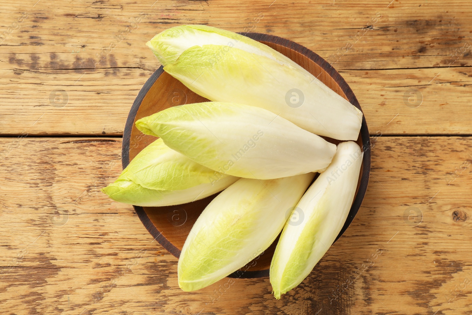 Photo of Fresh raw Belgian endives (chicory) in bowl on wooden table, top view