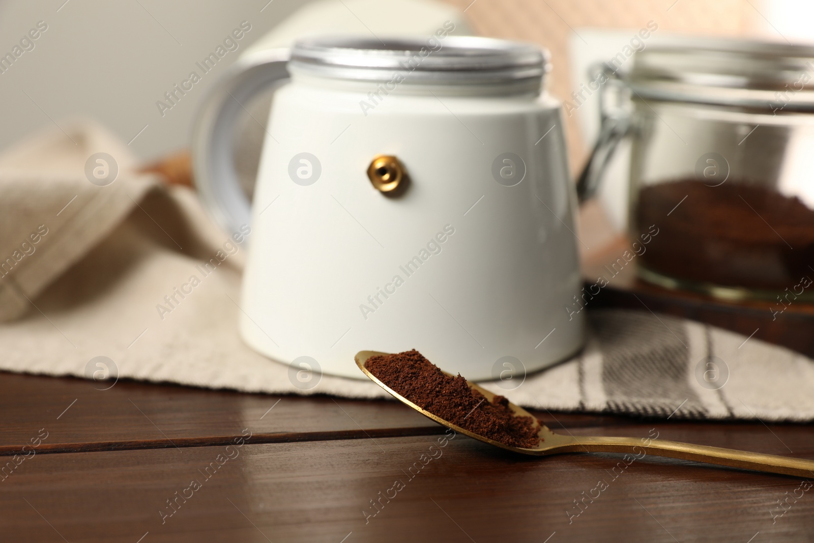 Photo of Moka pot and spoon with ground coffee on wooden table, closeup