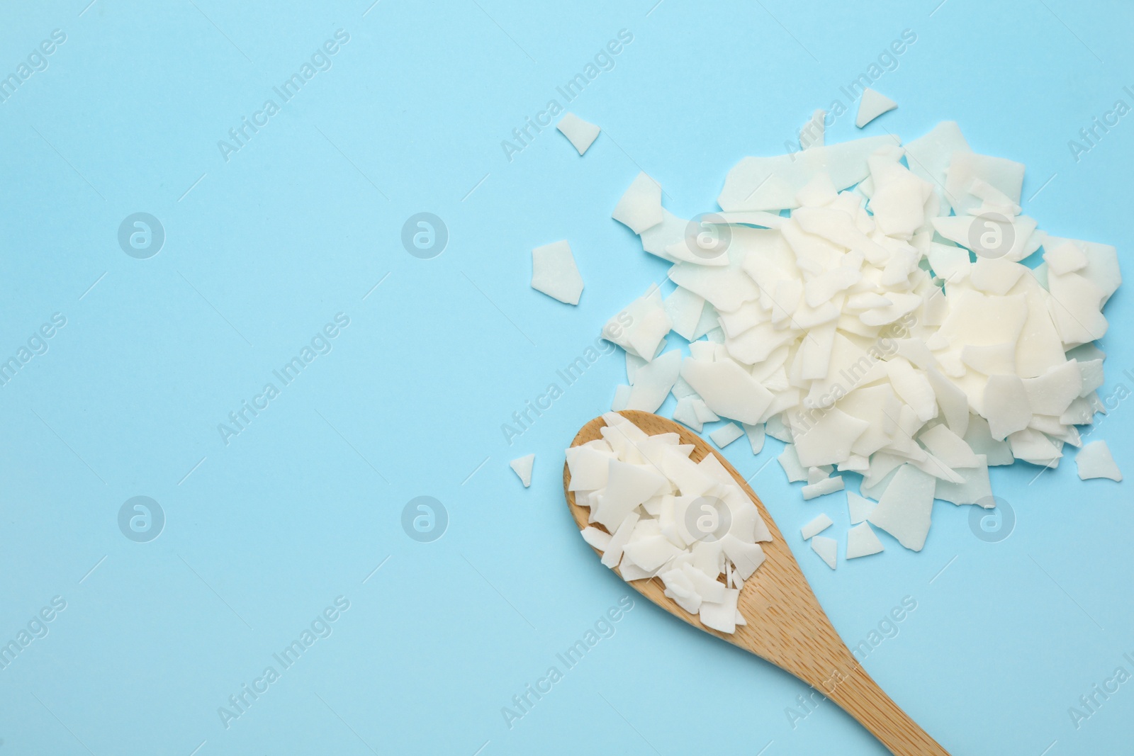 Photo of Wooden spoon and soy wax flakes on light blue background, flat lay with space for text. Homemade candle material
