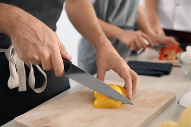 Photo of Male chef cutting paprika on wooden board at table, closeup