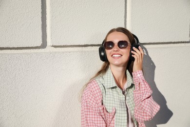 Photo of Smiling woman in headphones listening to music near white wall outdoors. Space for text