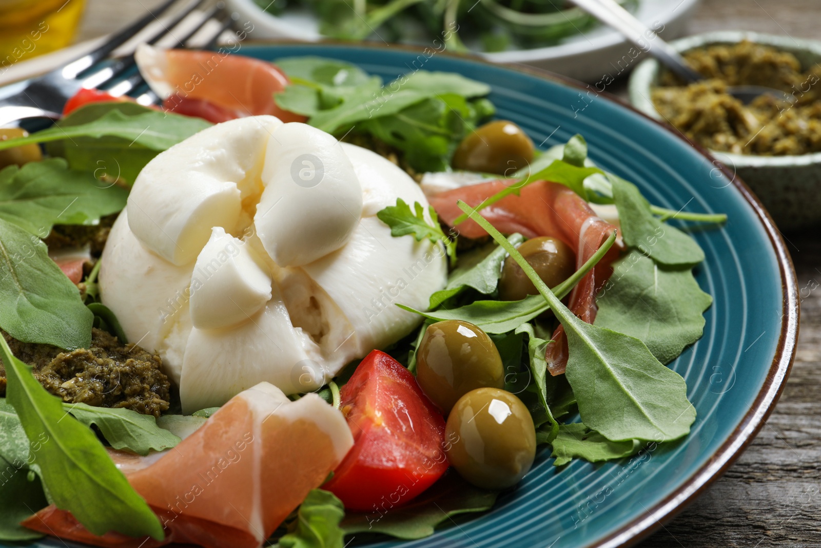 Photo of Delicious burrata salad served on wooden table, closeup