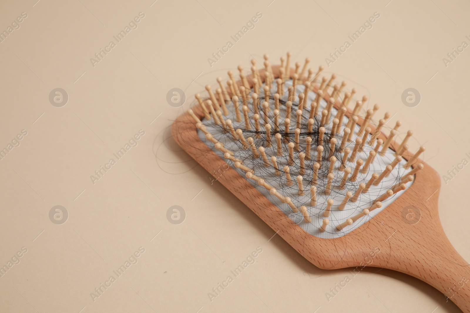 Photo of Wooden brush with lost hair on beige background, closeup. Space for text