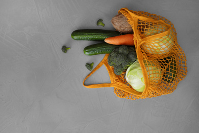 Photo of Net bag with vegetables on light grey table, flat lay. Space for text