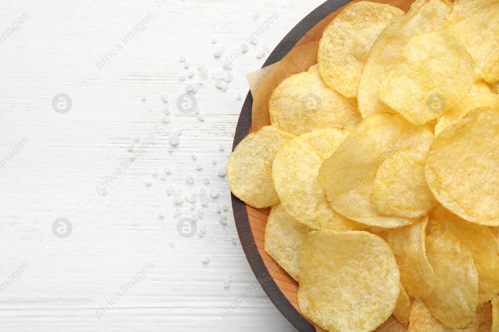 Photo of Delicious crispy potato chips in bowl on table, top view with space for text