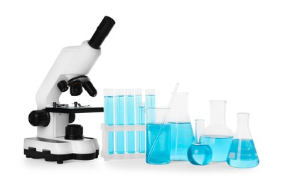 Photo of Laboratory glassware with light blue liquid and microscope isolated on white