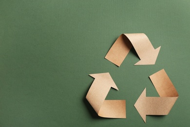 Photo of Recycling symbol cut out of kraft paper on green background, top view. Space for text