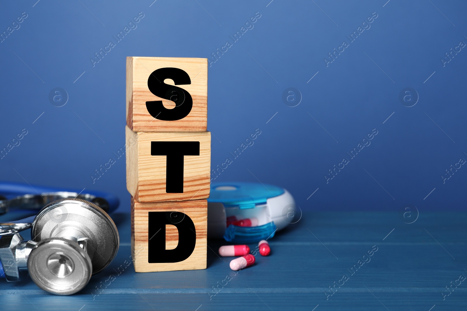 Photo of Wooden cubes with letters STD, capsules and stethoscope on blue table, space for text