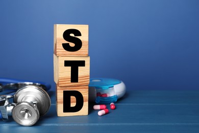 Photo of Wooden cubes with letters STD, capsules and stethoscope on blue table, space for text