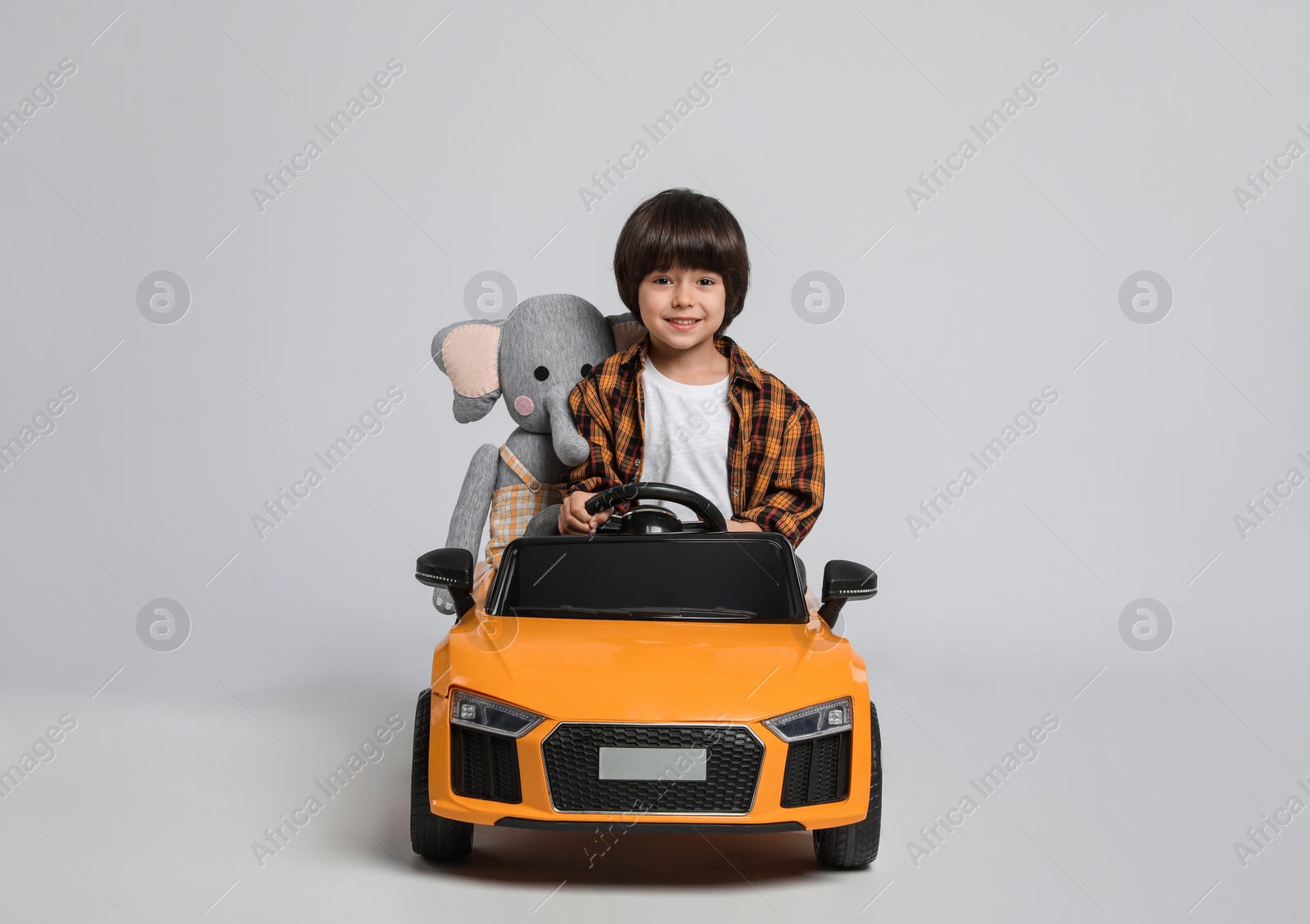 Photo of Cute little boy with toy elephant driving children's car on grey background