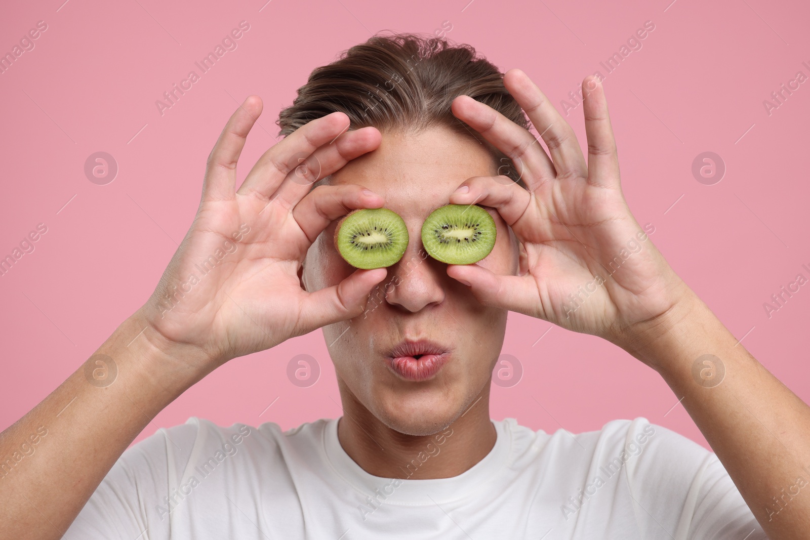 Photo of Man covering eyes with halves of kiwi on pink background, closeup