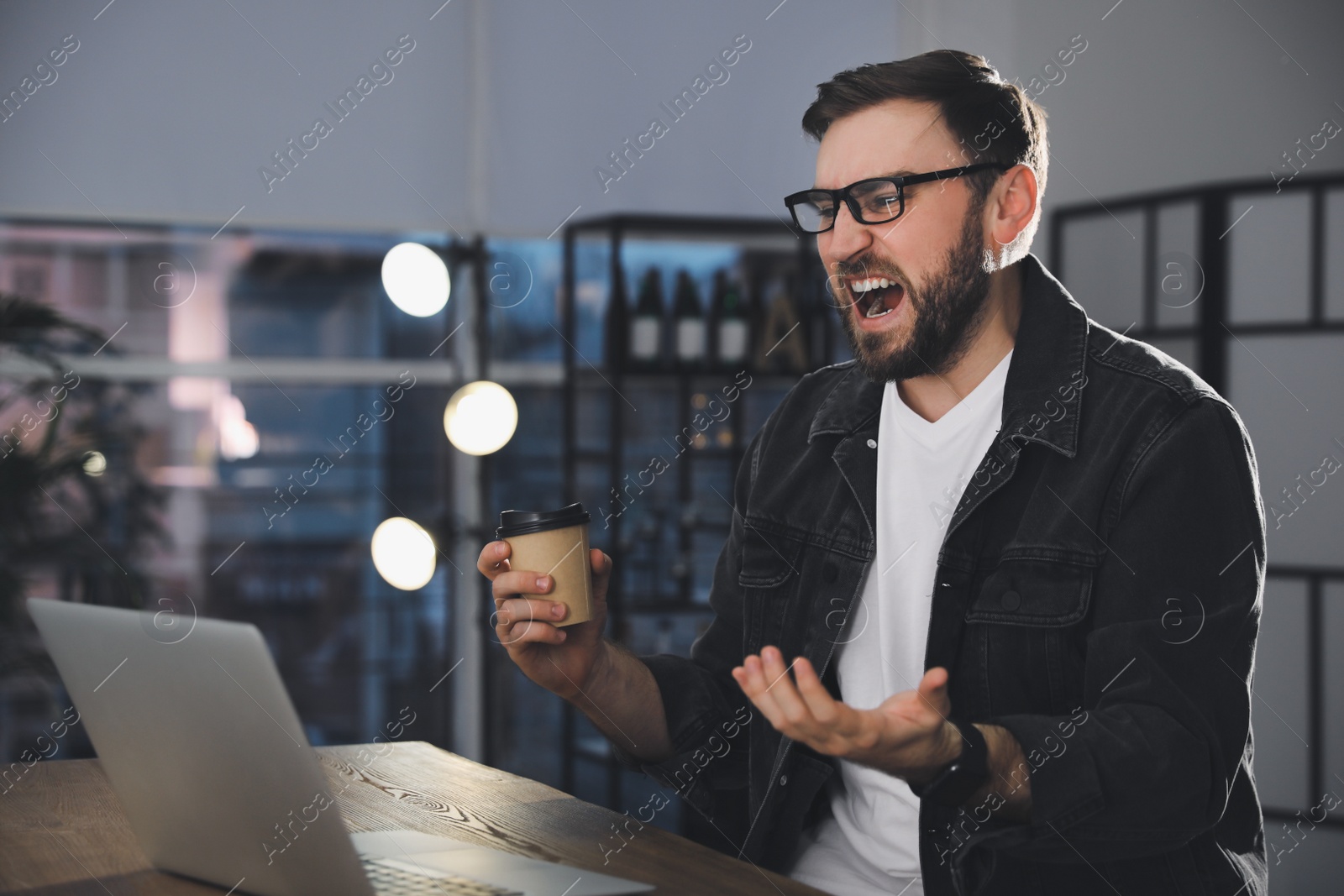 Photo of Emotional young man working on laptop in office. Online hate concept