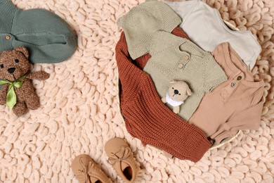 Photo of Laundry basket with baby clothes, shoes and crochet toys on beige rug, flat lay