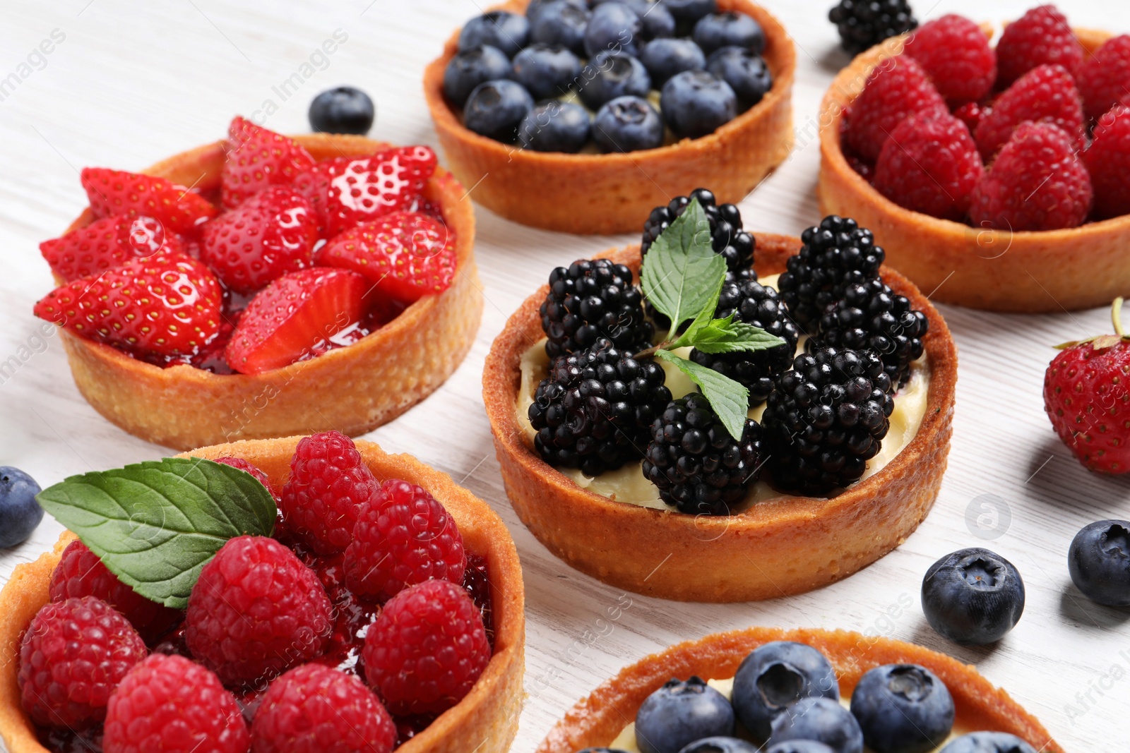 Photo of Tartlets with different fresh berries on white wooden table, closeup. Delicious dessert