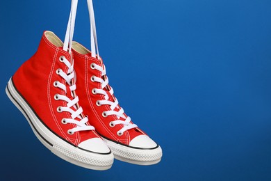 Pair of new stylish red sneakers hanging on laces against blue background. Space for text
