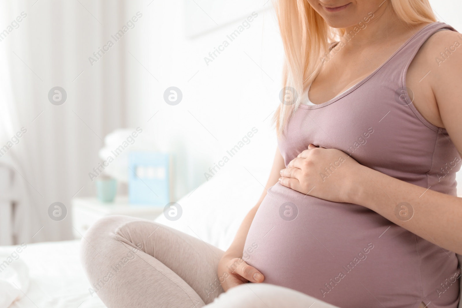 Photo of Pregnant woman sitting on bed in light room. Space for text