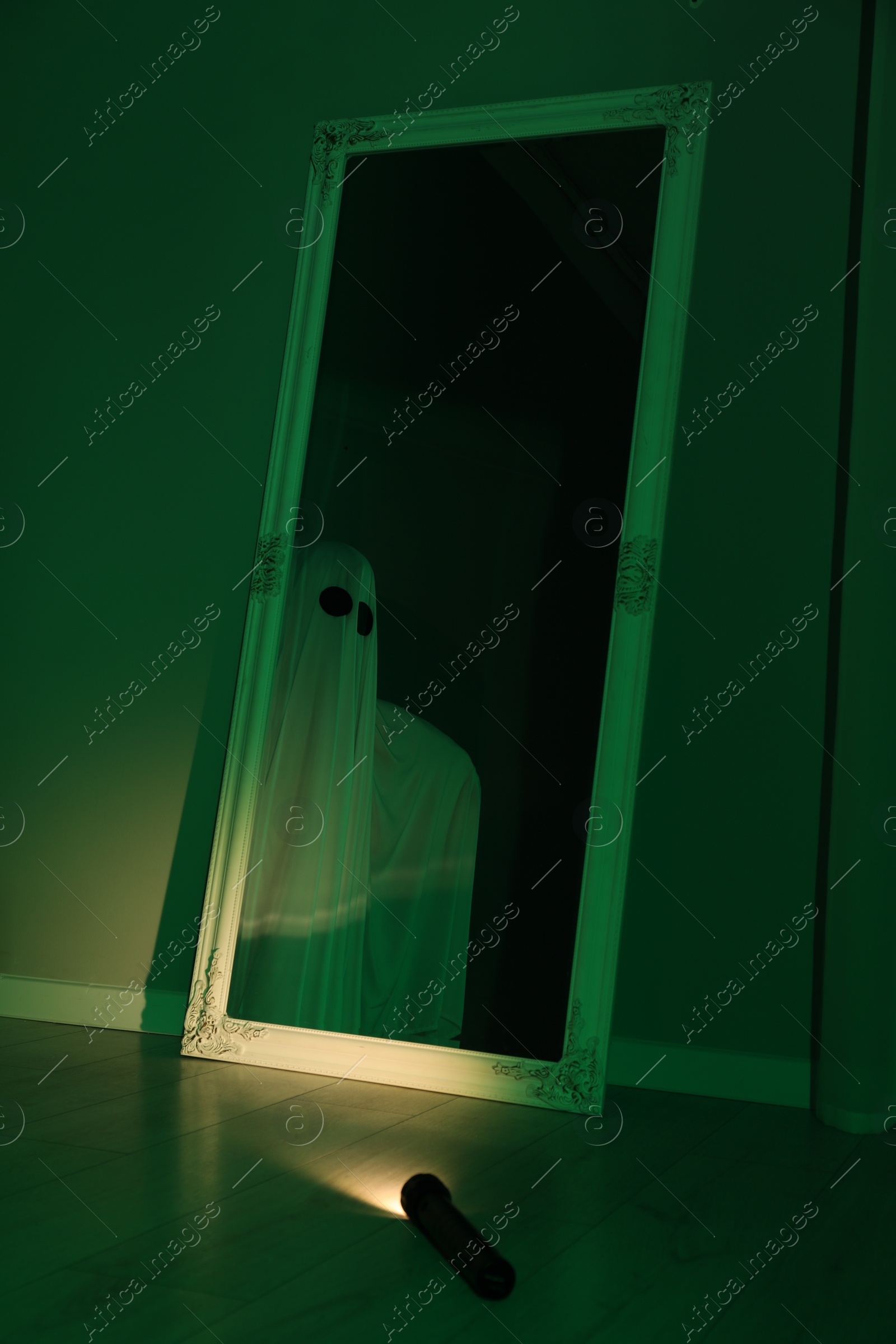 Photo of Creepy ghost. Woman covered with sheet in green light, reflection in mirror