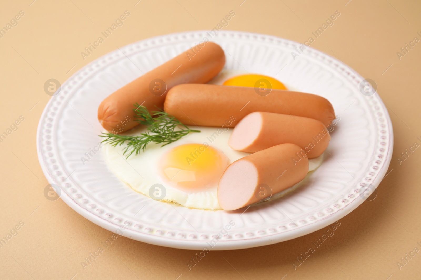 Photo of Delicious boiled sausages, fried eggs and dill on beige background, closeup