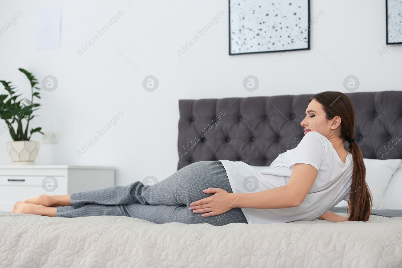 Photo of Young woman suffering from hemorrhoid on bed at home