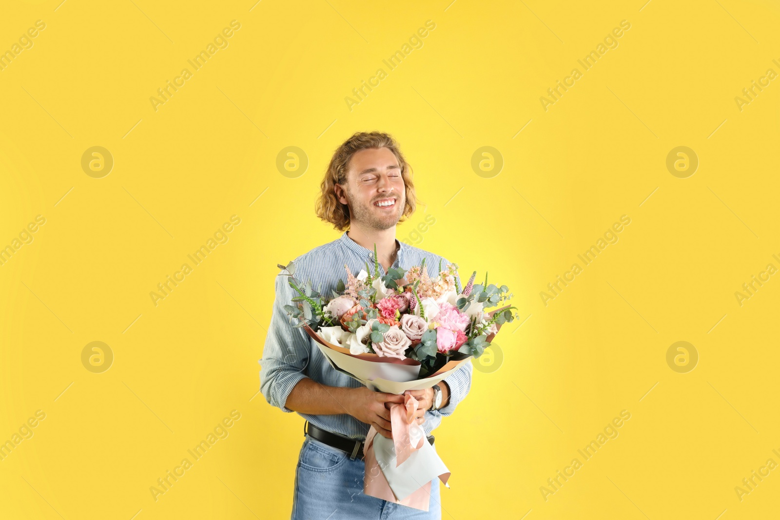 Photo of Young handsome man with beautiful flower bouquet on yellow background