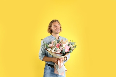 Young handsome man with beautiful flower bouquet on yellow background