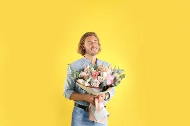 Photo of Young handsome man with beautiful flower bouquet on yellow background