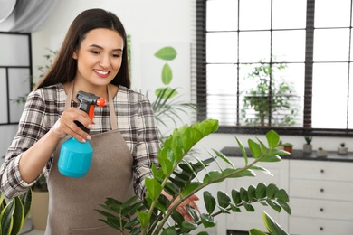 Young woman spraying plant with water at home