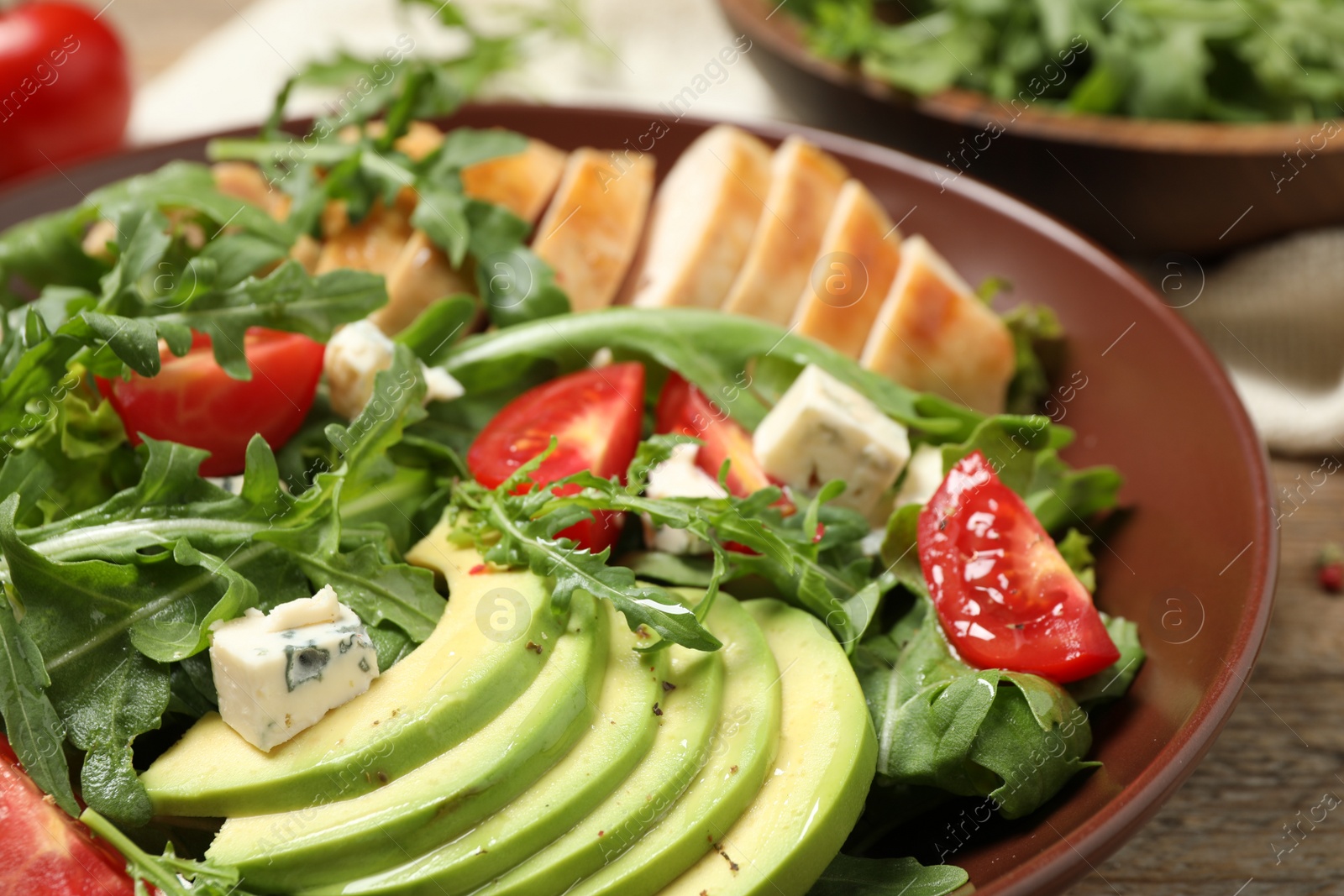 Photo of Delicious salad with chicken, arugula and avocado in bowl, closeup