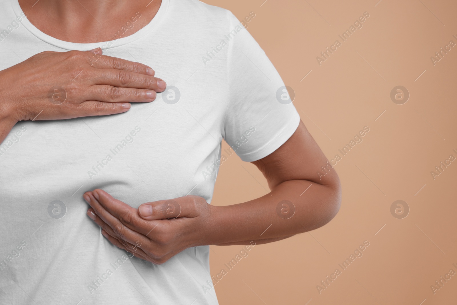 Photo of Woman doing breast self-examination on light brown background, closeup. Space for text