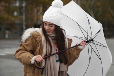 Woman with white umbrella caught in gust of wind on street