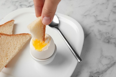 Photo of Woman dipping bread into soft boiled egg on table, closeup. Space for text