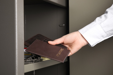 Photo of Woman putting passports into steel safe, closeup
