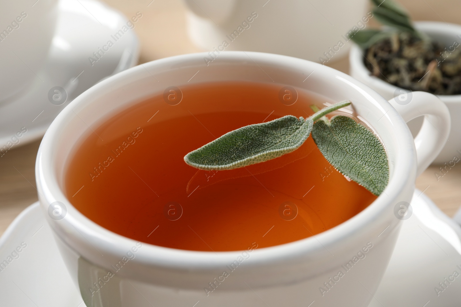 Photo of Cup of aromatic sage tea with fresh leaves on table, closeup