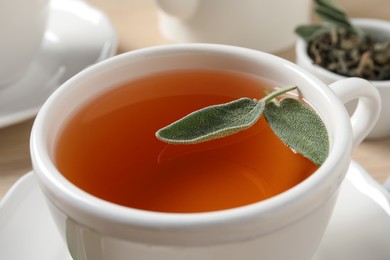 Photo of Cup of aromatic sage tea with fresh leaves on table, closeup